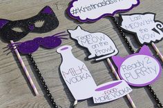 some purple and black party decorations on a wooden table with cat masks, wine bottles, and candy sticks