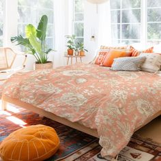 a bed with orange and white pillows in a room next to two large potted plants