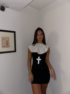 a woman in a black and white dress standing next to a wall with a cross on it