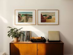 two pictures hang on the wall above a wooden cabinet with an old radio and record player