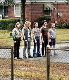 a group of people standing in front of a house on a sidewalk next to a fence