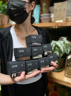 a woman wearing a black face mask and holding up nine boxes of tattie