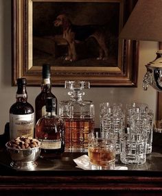 a table topped with bottles and glasses filled with liquor next to a painting on the wall