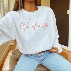 a woman sitting on top of a chair wearing a white sweater with cleveland written on it