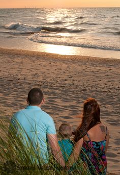 a man and woman sitting on top of a sandy beach next to the ocean at sunset