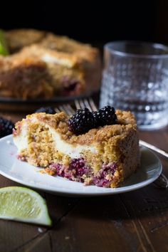 a piece of cake on a white plate with blackberries and limes next to it