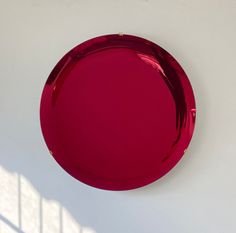 a red plate sitting on top of a white wall next to a shadow cast window