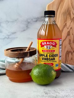 a bottle of apple cider vinegar sitting next to a lime and a wooden spoon