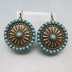 These pretty Mandala shaped earrings are inlaid with pieces of fairly realistic looking faux turquoise set into goldtone metal. They measure  2 inches long (including the wires)  and 1 5/8th inch wide . They have a mandala, wagon wheel design and are light and comfortable on.  They are in MINT condition with no markings. This will arrive in a lovely gift box for easy gift giving or safe storage.  For more pieces of vintage costume jewelry, old silver, bolo ties and vintage accessories, kindly ch Turquoise Beaded Brass Jewelry, Turquoise Brass Jewelry With Ear Wire, Handmade Southwestern Gold Earrings, Turquoise Concho Dangle Jewelry, Southwestern Concho Earrings For Festivals, Turquoise Beaded Earrings With Metal Ear Wire, Blue Concho Dangle Earrings, Southwestern Style Gold Earrings For Gifts, Southwestern Style Gold Earrings For Gift