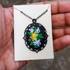 a hand holding a black and white necklace with colorful flowers on it's chain