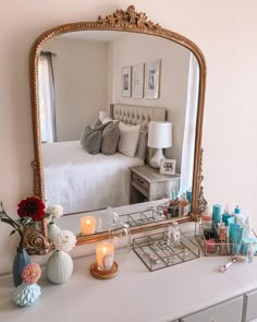 a white dresser topped with a mirror and vase filled with flowers next to a bed