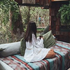 a woman sitting on top of a bed next to a tree house in the woods