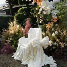 a white chair sitting in the middle of a flower garden next to a tall tree