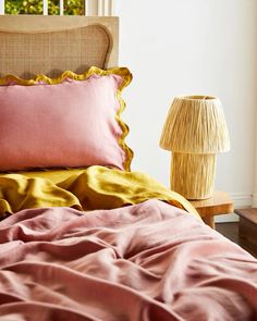 a bed with pink and yellow sheets in a bedroom next to a lamp on a table