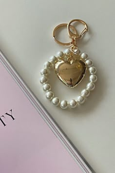 These keychains showcase a chunky puff heart metallic charm suspended from a chubby pearl beaded chain. With its unique design, this keychain adds a touch of style and sentiment to your everyday essentials. Carry your keys with a touch of love and flair, or attach them to your bag for a fashionable statement. The combination of the heart charm and the dainty pearls creates a harmonious blend of sophistication and playfulness. Please be aware that the charm is intentionally designed to have a bol Keychain Charms Aesthetic, Cute Keys Aesthetic, Gold Pearl Jewelry With Heart Charm, Pearl Key Chain, Heart-shaped Pearl Charm Earrings As Gift, Bead Keychain, Heart-shaped Pearl Charm Jewelry, Luxury Bag Charm With Keychain, Modern Henna Designs