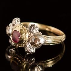 This amazing ring hails from the Georgian era of jewelry (c. 1715-1800). At its center lies a beautiful, rose-red ruby fashioned into a table cut, one of the oldest known gemstone faceting patterns. Flanking the ruby’s decoratively textured 22k yellow gold bezel, six exquisite rose-cut diamonds sparkle mysteriously from within their closed-back silver settings. The ring is crafted of sterling silver and 14k yellow gold, with a 22k yellow gold setting around the central stone. The table-cut ruby Antique Ruby Ring With Single Cut Diamonds, Victorian Ruby Jewelry With Single Cut Diamonds, Antique Ruby Rings With Single Cut Diamonds, Antique Red Diamond Ring With Rose Cut Diamonds, Antique Hallmarked Ruby Ring, Antique Red Diamond Ring With Gemstone, Antique Red Gemstone Diamond Ring, Antique Ruby Ring With Rose Cut Diamonds, Victorian Ruby Ring With Single Cut Diamonds