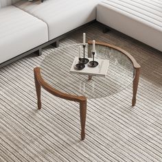 a glass table with two candles on it in front of a white couch and coffee table