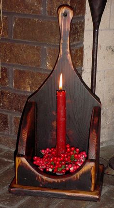 a candle is lit in a wooden holder with red berries on the floor next to a brick wall