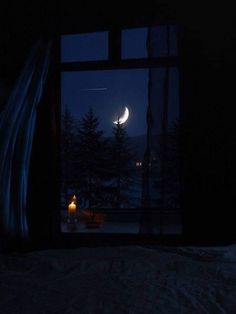 the moon is seen through an open window at night with candles lit in front of it