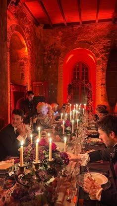 a group of people sitting around a dinner table with candles in the middle of it