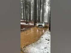 a car driving through a muddy road in the woods with snow on the ground and trees