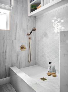 a white tiled bathroom with hexagonal tiles and gold faucet shower head