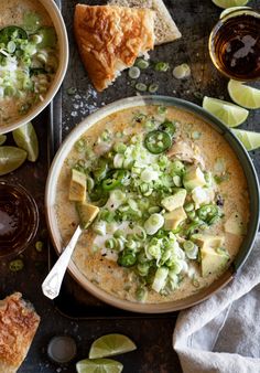 two bowls filled with soup next to slices of bread and limes on the side