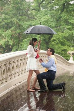 a man kneeling down next to a woman holding an umbrella