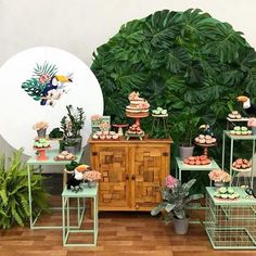 a table topped with cakes and cupcakes next to a green plant covered wall