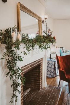 a fireplace with candles and greenery on it in a living room next to a mirror