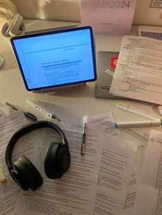 a computer monitor sitting on top of a desk next to headphones and paper work