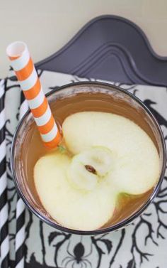 an apple drink in a glass with two orange and white striped straws on the table