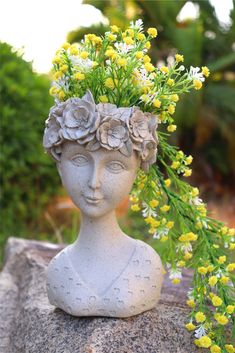 a statue with flowers in its hair on top of a rock