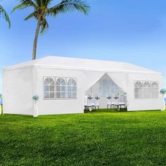 a large white tent set up on top of a lush green field next to a palm tree