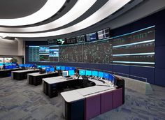 an empty control room with multiple monitors on the wall and desks in front of them