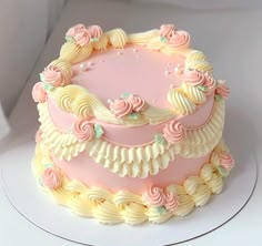 a pink and yellow cake with flowers on it sitting on a white tableclothed surface