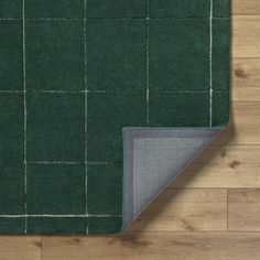 a green rug on top of a wooden floor next to a gray area rug with white squares