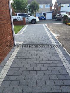 a brick walkway leading to a house with cars parked in the driveway and on the other side