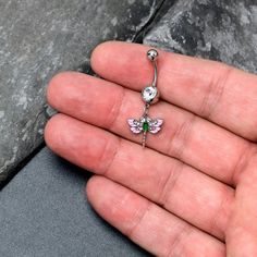 a person holding a tiny pink and green butterfly navel bar on their left hand