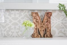 a wooden letter sitting on top of a white shelf next to a vase filled with flowers