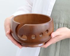 a woman holding a wooden bowl with holes in the center and two hands on it