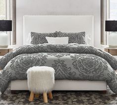 a white bed sitting next to two windows in a bedroom with gray and white decor