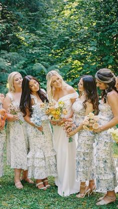 a group of women standing next to each other in front of green grass and trees