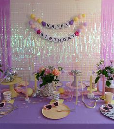 a purple table topped with plates and cups filled with flowers next to a happy birthday banner