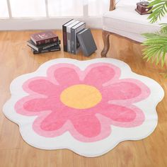 a pink and yellow flower rug sitting on top of a wooden floor next to books