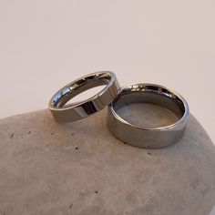 two silver wedding rings sitting on top of a stone slab in front of a white wall