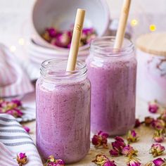 two mason jars filled with purple smoothie next to pink flowers on a white surface