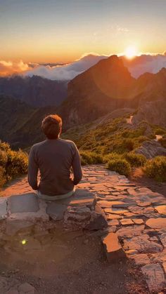 a man sitting on top of a stone walkway in the middle of a mountain at sunset