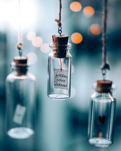 three glass bottles hanging from strings that say love is in the air and are filled with tiny hearts