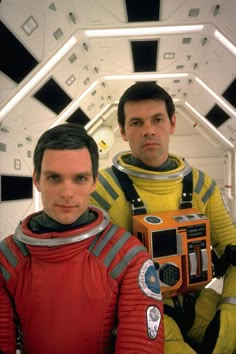 two men in space suits holding an old camera